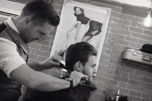 Black and white side on photo of a barber combing a clients hair