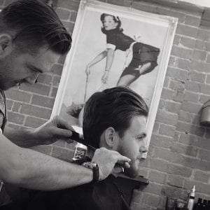 Black and white side on photo of a barber combing a clients hair