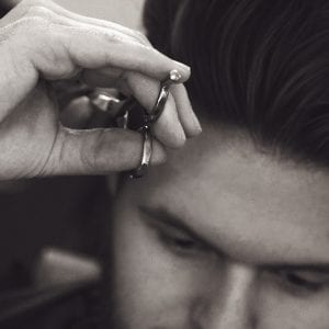 A close up photo of a barber using scissors to cut a client hair